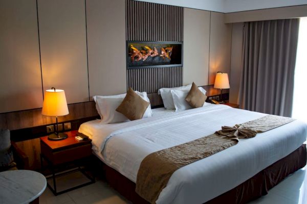 A cozy hotel room with a large, neatly made bed, decorative pillows, bedside lamps, and wall art above the headboard.