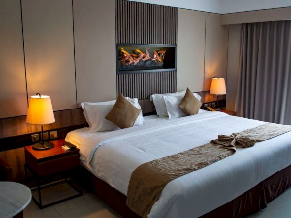 A cozy hotel room with a large, neatly made bed, decorative pillows, bedside lamps, and wall art above the headboard.
