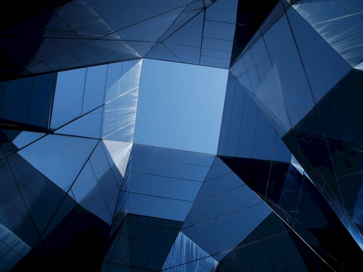 Geometric architecture with mirrored surfaces creating a kaleidoscopic effect and an open sky visible in the center.