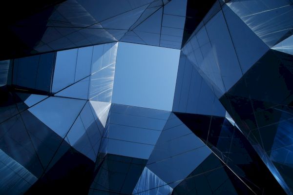 Abstract view of modern glass buildings reflecting light, forming a geometric pattern with a clear blue sky at the center.