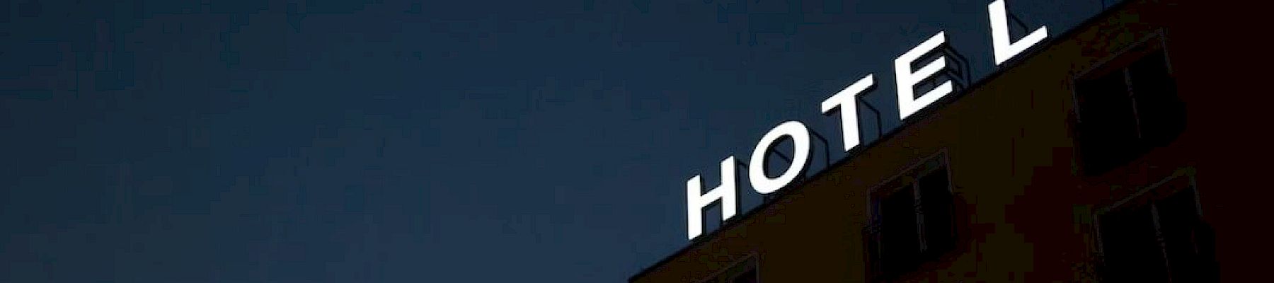 A building at night with an illuminated "HOTEL" sign on the roof, missing the letter "H" leaving "OTEL" visible.