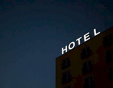 A building at night with an illuminated "HOTEL" sign on the roof, missing the letter "H" leaving "OTEL" visible.