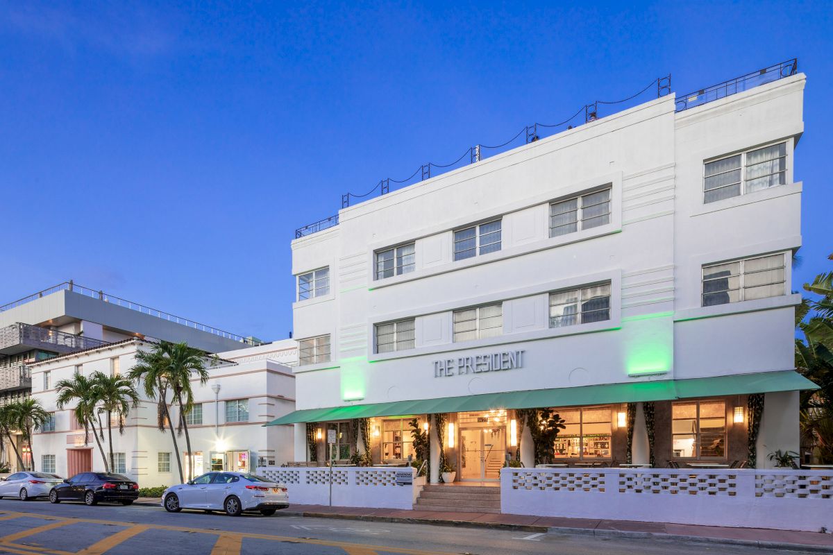 A white, multi-story building with a green awning and palm trees in front of it.