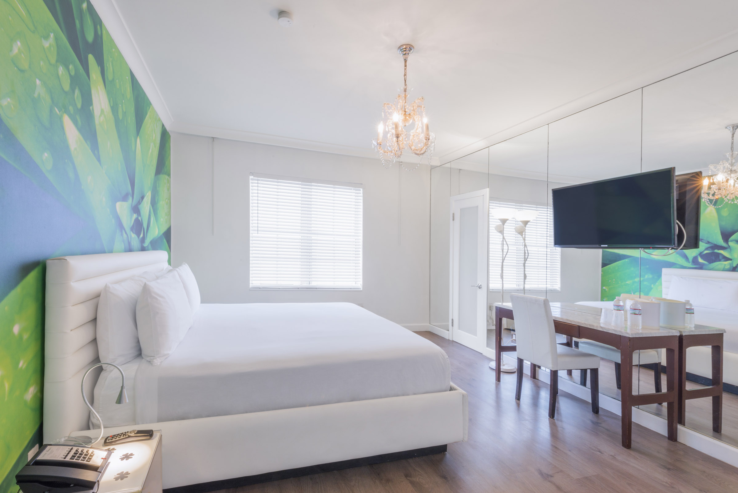 A wide view of a hotel room with a bed, TV, desk, and chandelier.