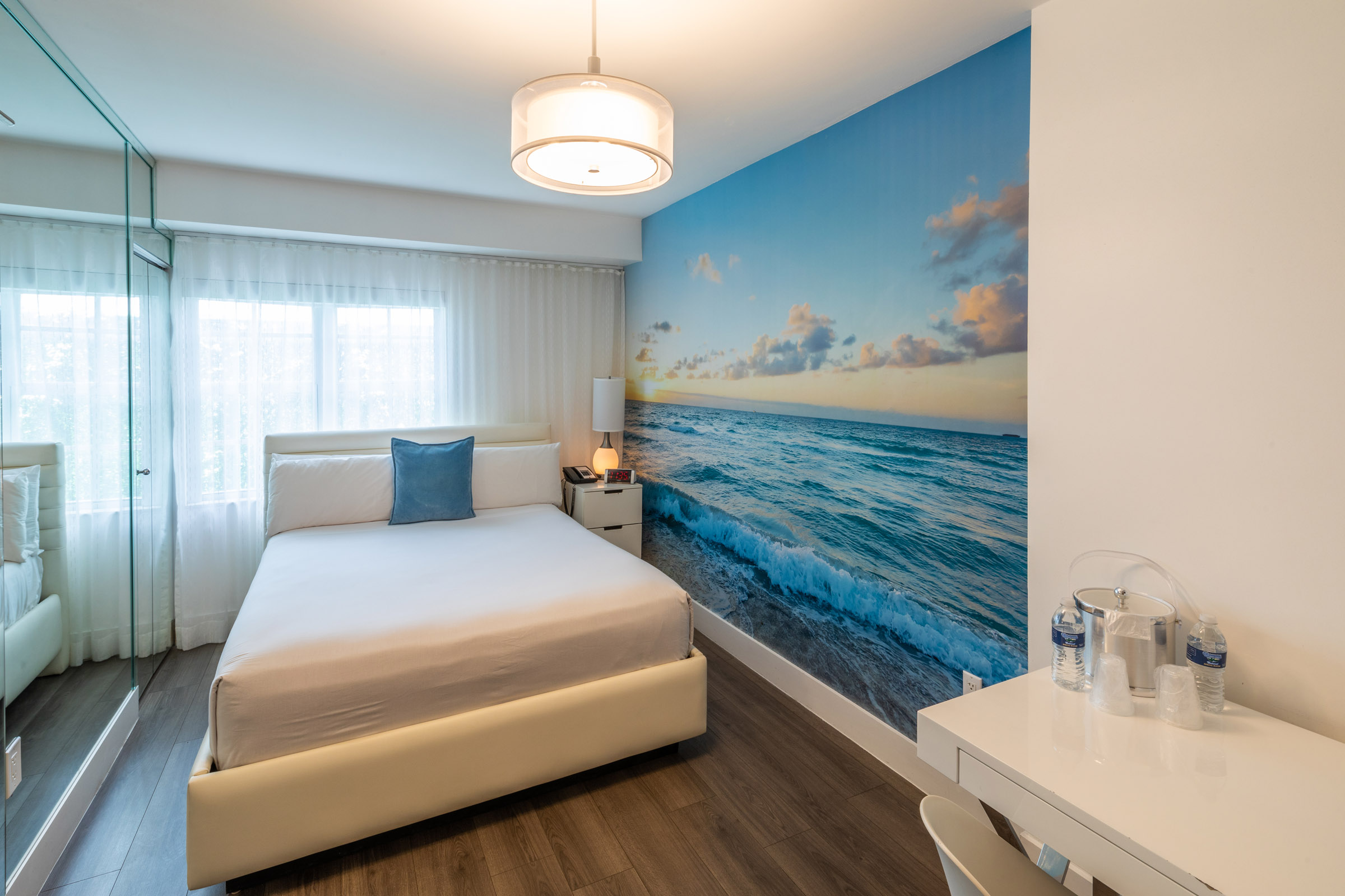 A hotel room with a large ocean mural, a bed, a desk, and a mirror.