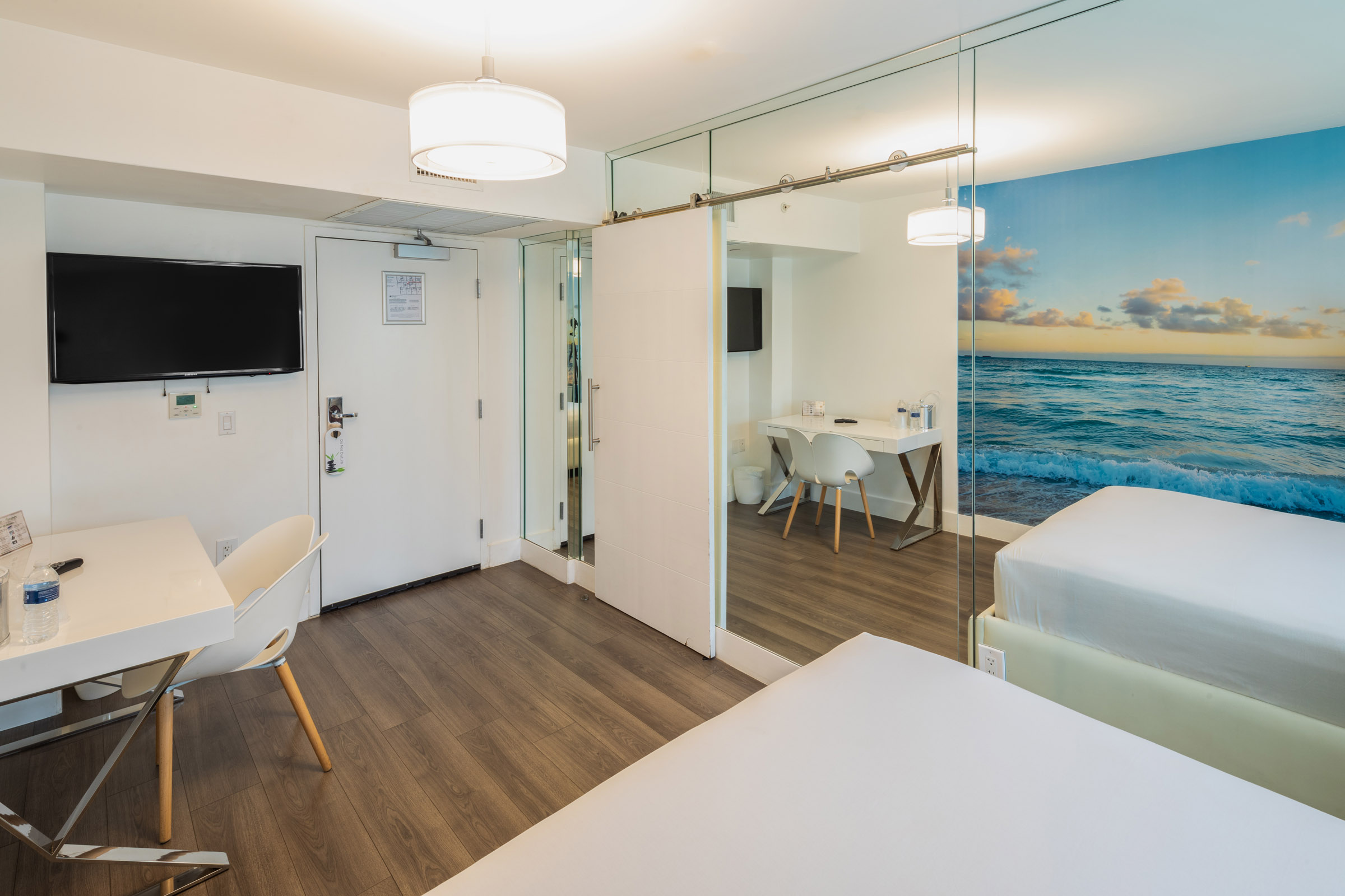 A hotel room with a bed, desk, TV, and mirror.