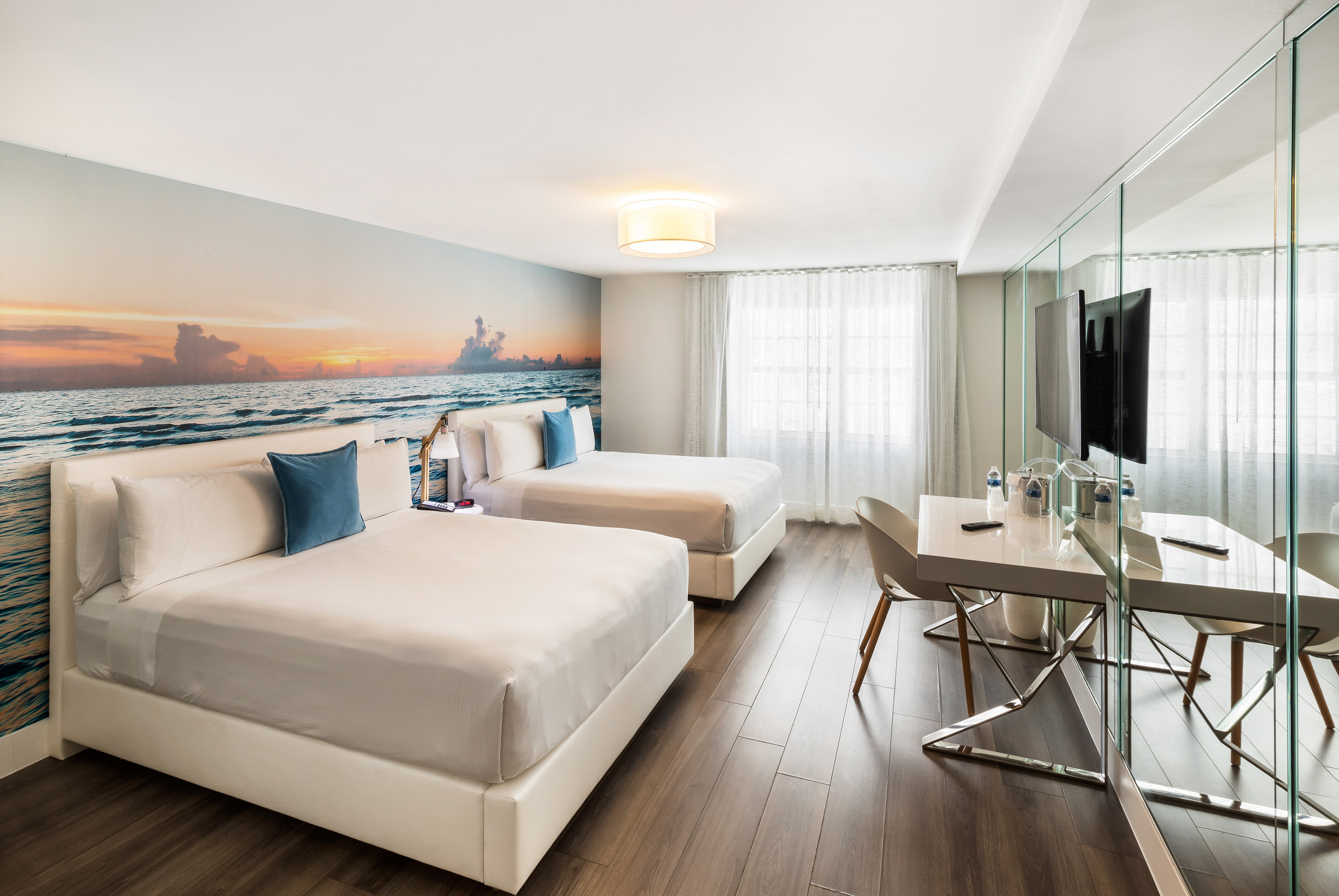 A hotel room with two beds, a desk, and a TV.