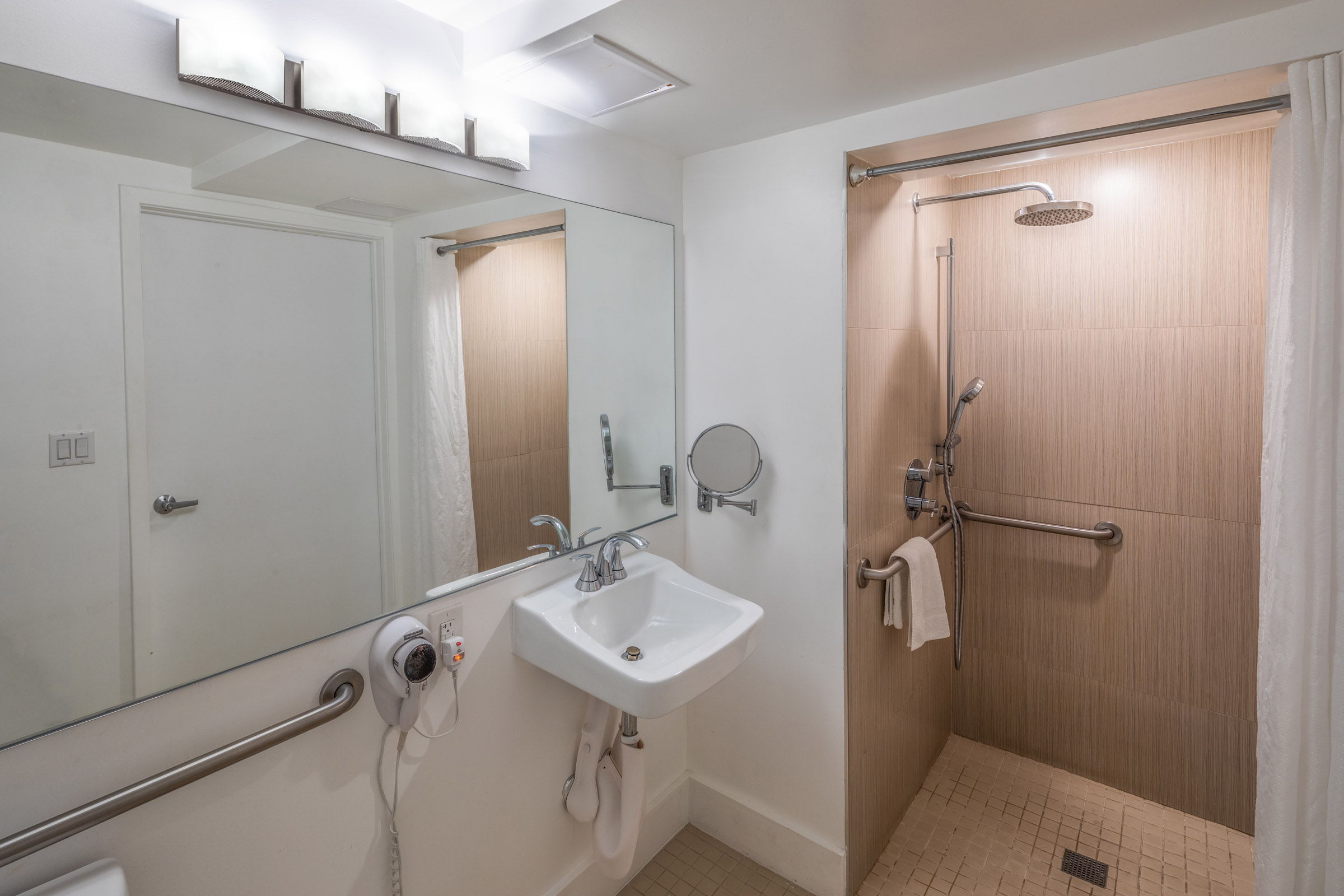 A clean and modern bathroom with a shower, single sink, and grab bars.