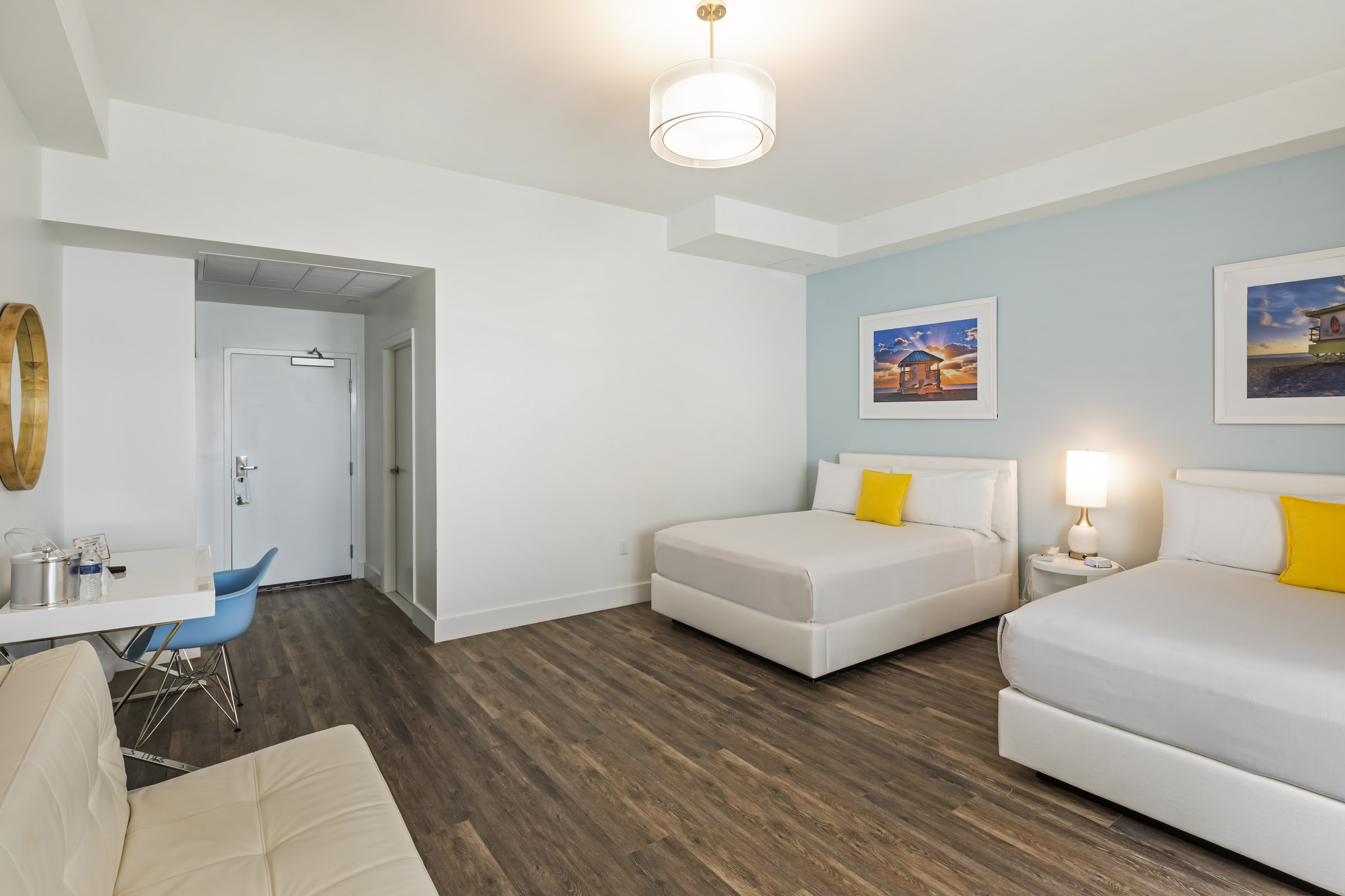 A hotel room with two beds, a desk, a couch, and artwork on the walls.
