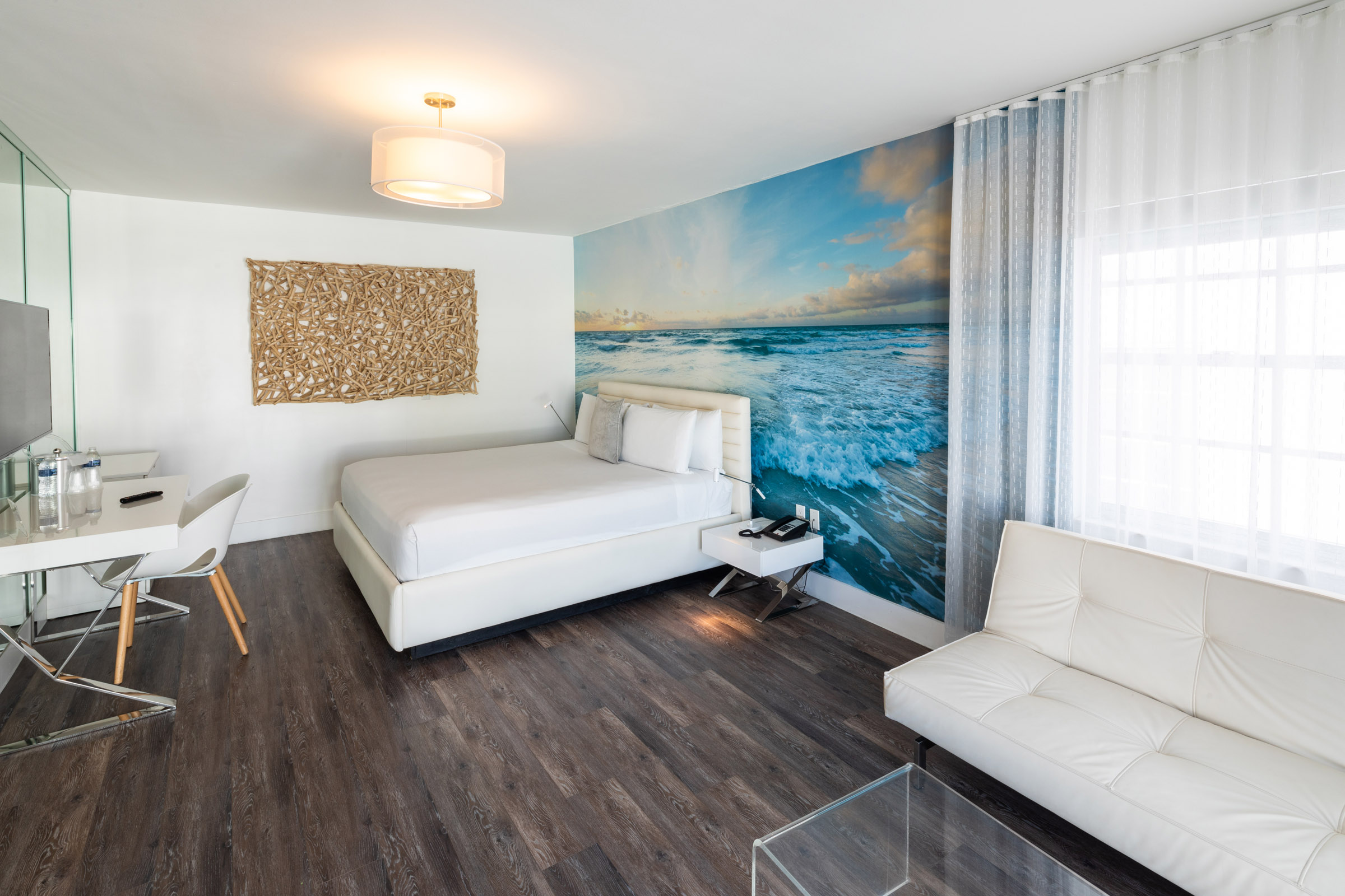 A hotel room with a white bed, sofa, and desk.