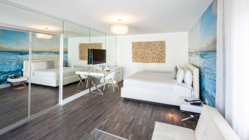 A wide view of a hotel room with a bed, desk, mirror, and TV.