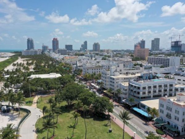 Aerial view of a coastal city with skyscrapers, green parks, and beaches under a blue sky with clouds.
