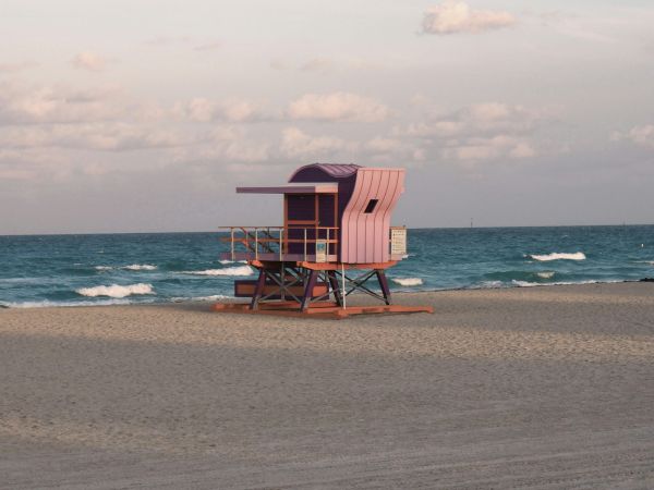 A colorful lifeguard tower on a sandy beach by the ocean under a partly cloudy sky at sunset.