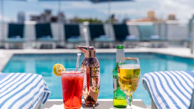 A poolside scene with drinks and towels on lounge chairs.