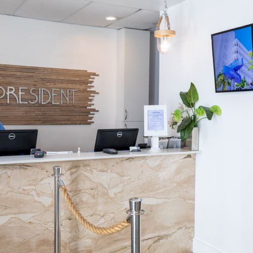 A front desk labeled "PRESIDENT" with a staff member on the phone and a screen displaying information about Lincoln Road Mall.