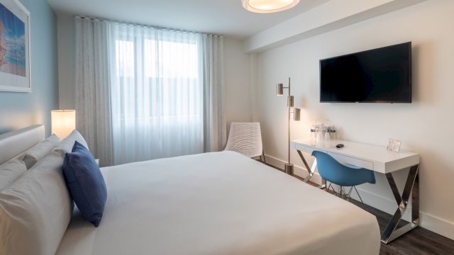 A wide view of a hotel room with a large bed, desk, TV, and window.