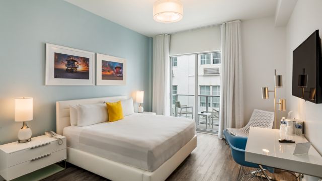 A clean and modern hotel room with a bed, desk, TV, and balcony.