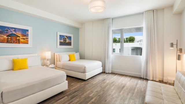 A wide view of a hotel room with two beds, a window, and artwork on the wall.