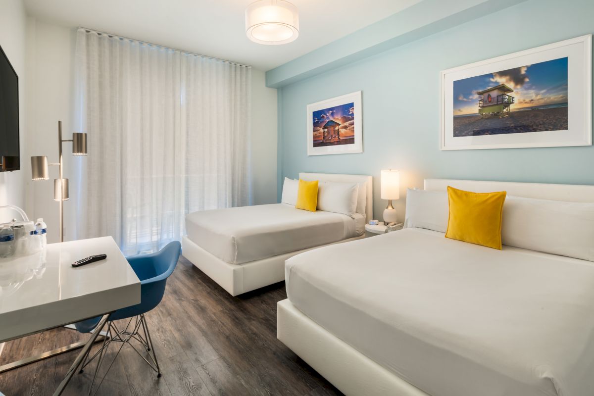 A hotel room with two beds, a desk, and a blue accent wall.