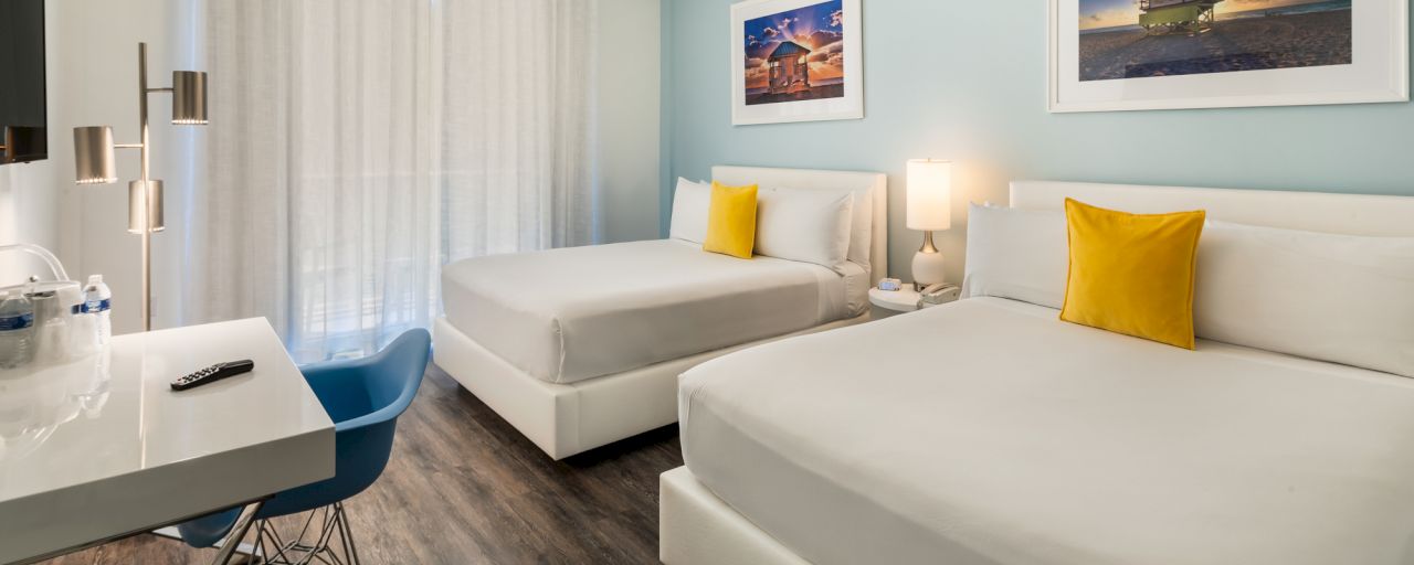 A hotel room with two beds, a desk, and a chair.