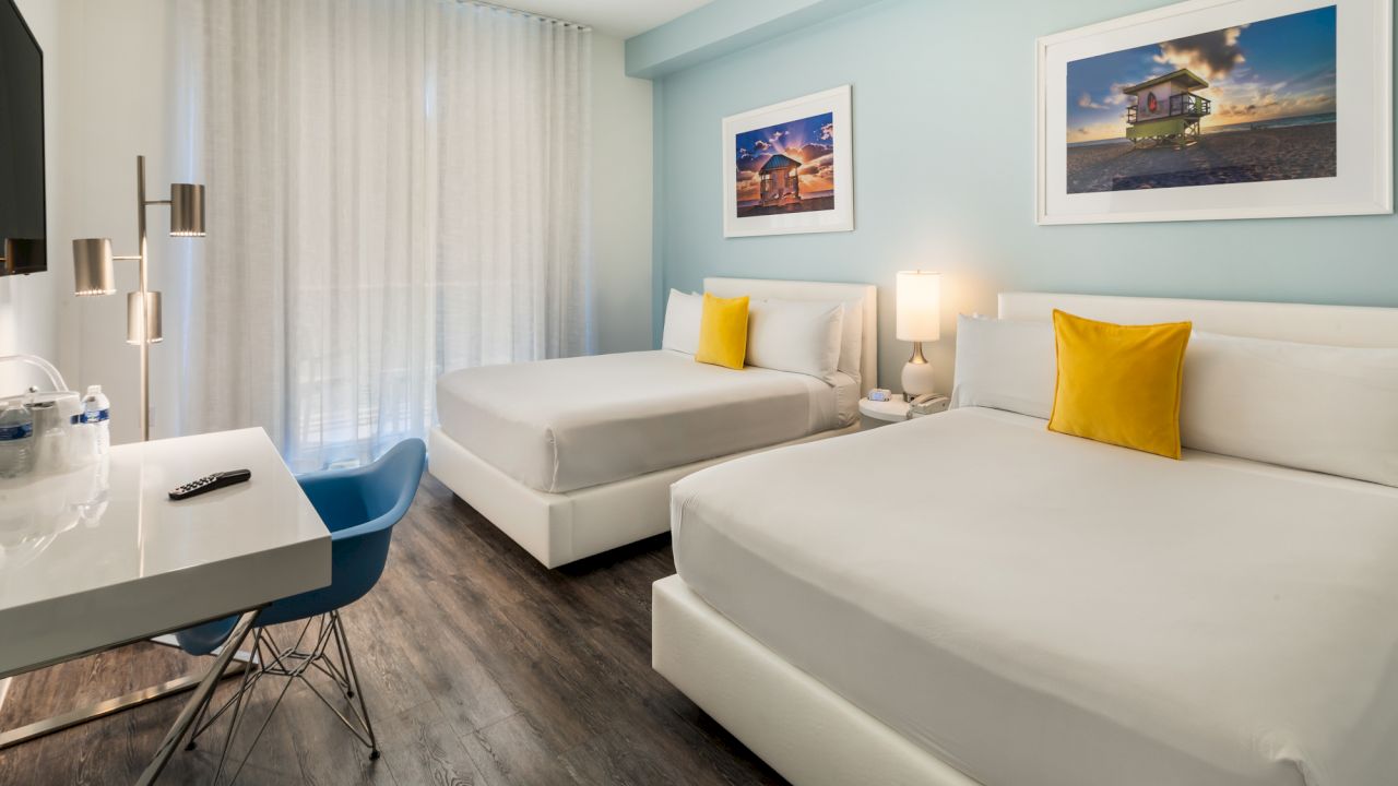 A hotel room with two beds, a desk, and artwork on the walls.