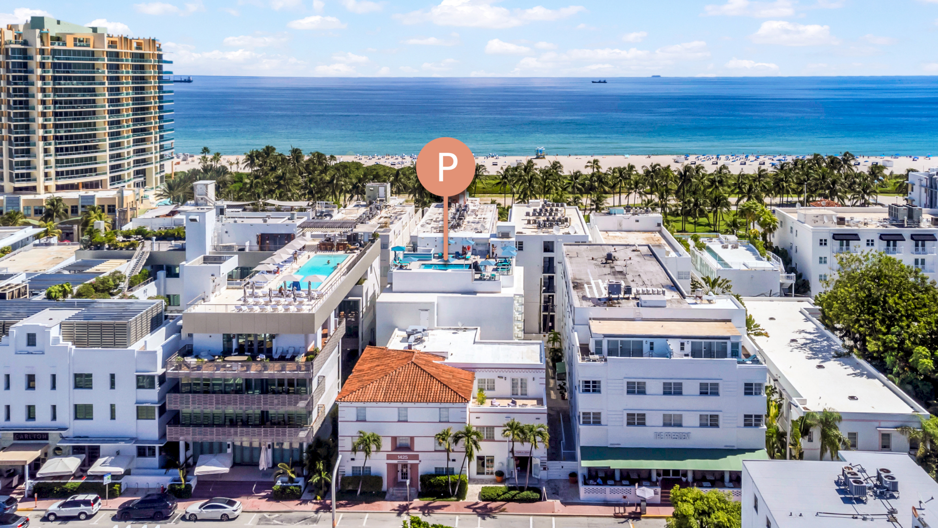 Aerial view of a coastal city with tall buildings, rooftops, and a "P" marker near the beach, with the ocean in the background.