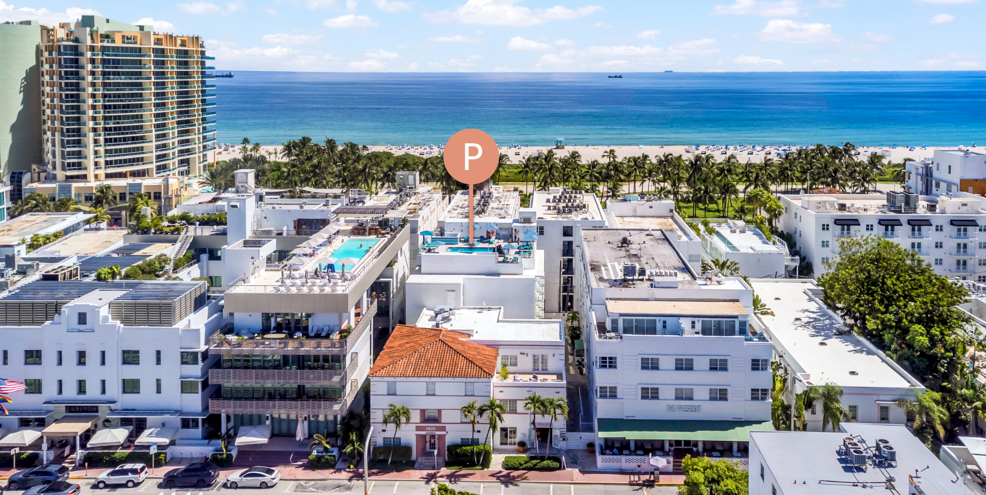 Aerial view of a coastal city with tall buildings, rooftops, and a "P" marker near the beach, with the ocean in the background.