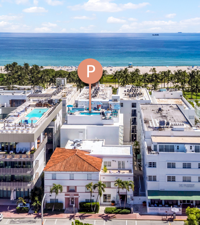 Aerial view of a hotel with a pool and parking lot near the beach