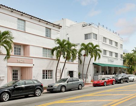 A sunny street with parked cars beside a white building and palm trees, with a “Beach” sign on the right.