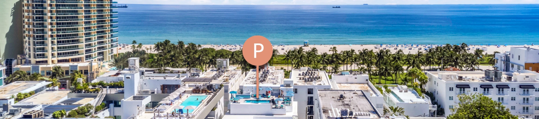 A bright oceanfront resort with palm trees, white buildings, and a sandy beach beside a calm blue sea under sunny clouds.