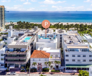 A bright oceanfront resort with palm trees, white buildings, and a sandy beach beside a calm blue sea under sunny clouds.