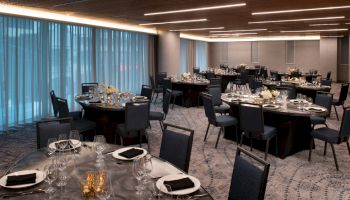 A banquet hall with round tables set for dining, elegant lighting, and neatly arranged chairs and tableware.