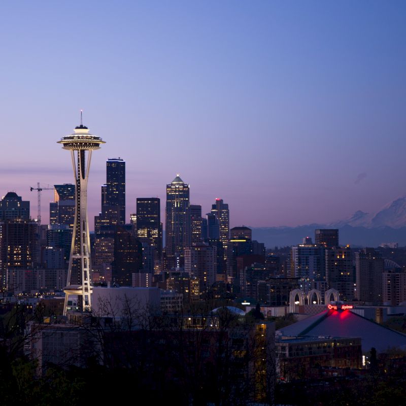 Seattle skyline at dusk with the Space Needle and Mount Rainier in the background under a twilight sky.