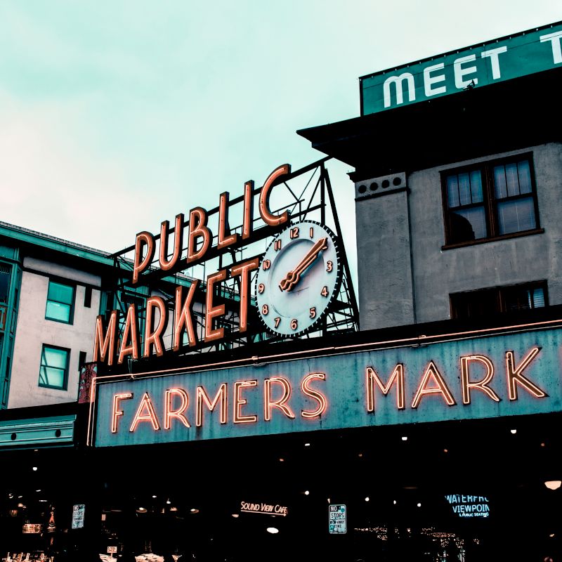 The image shows a famous market sign with "Public Market" and "Farmers Market" in neon lights and a clock.