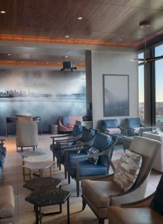 A modern lounge with chairs and couches, large windows with scenic views, and a cityscape mural on the wall.