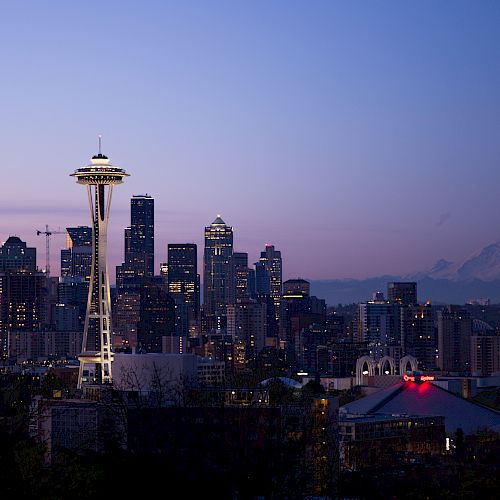 Seattle skyline at dusk featuring the Space Needle, city buildings, and Mount Rainier in the background under a clear sky.