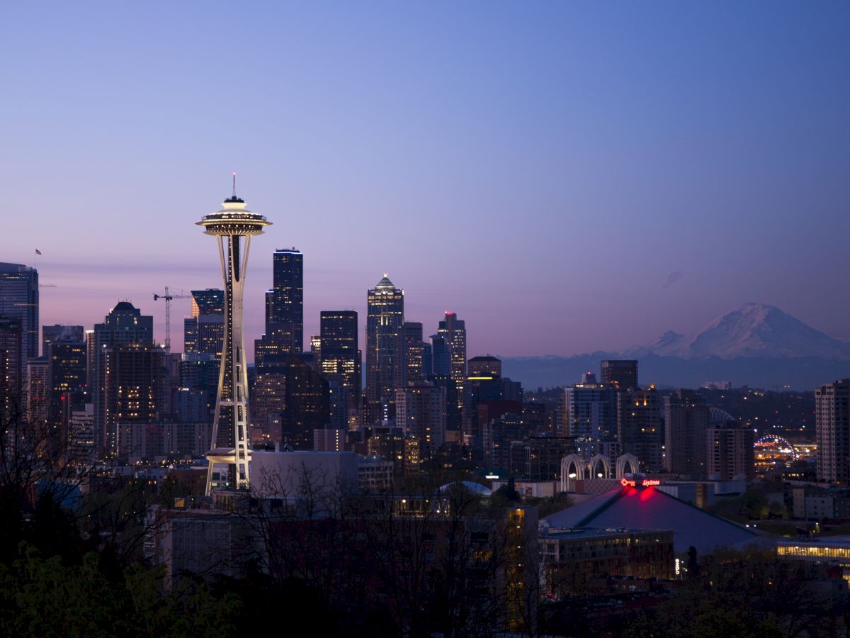 The image shows a skyline with the Space Needle in Seattle at dusk, along with city buildings and Mount Rainier in the background.