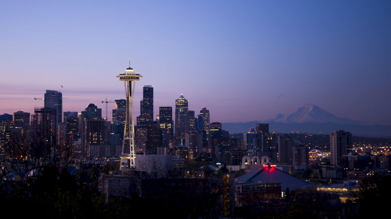 The image shows a skyline with the Space Needle in Seattle at dusk, along with city buildings and Mount Rainier in the background.